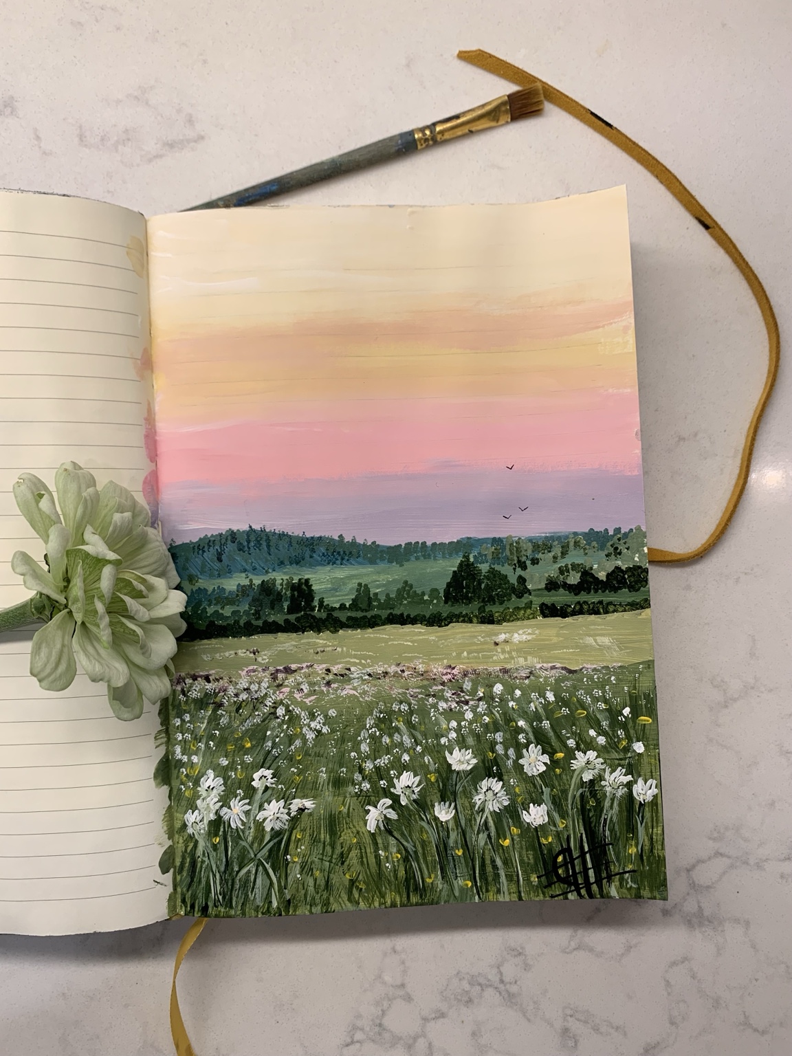 An open sketchbook with Christina's painted wildflower meadow, brush, and flower